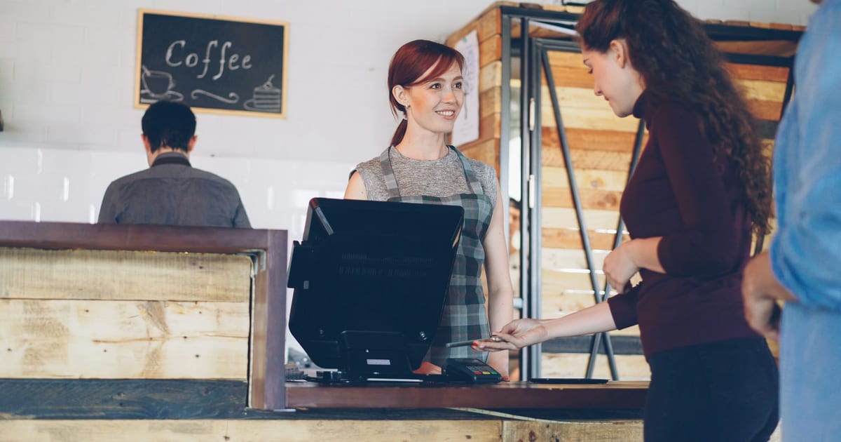 A customer paying at a coffee shop counter while the barista serves them.