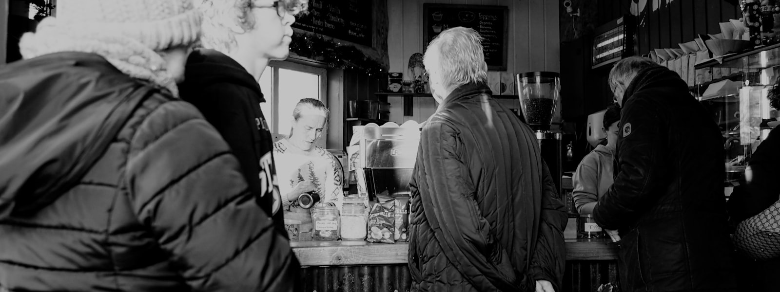 Customers waiting at the counter of a small independent coffee shop while the barista makes their order.