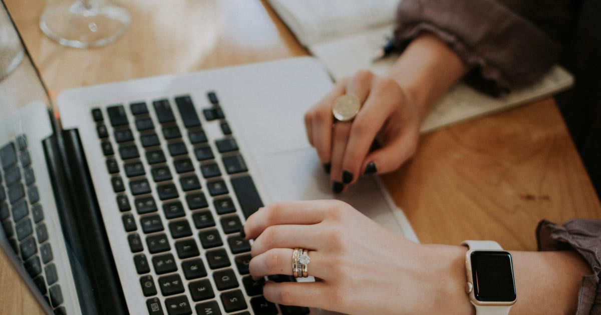 A small business owner's hands typing on a laptop beside an open notebook.