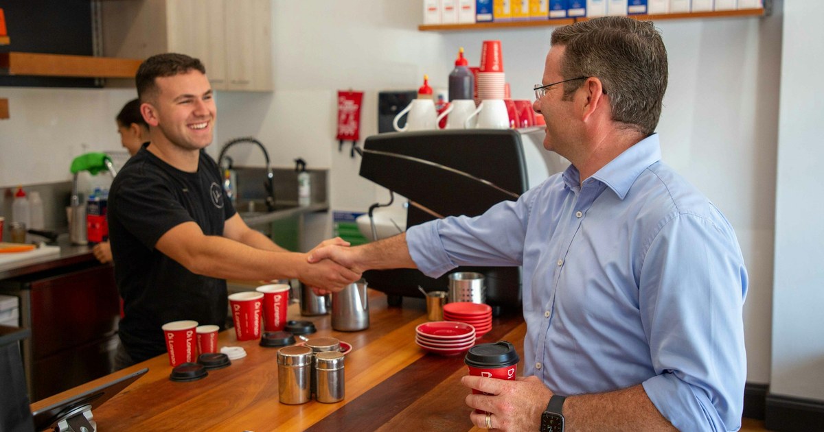 A barista shaking hands with a customer across a café counter.