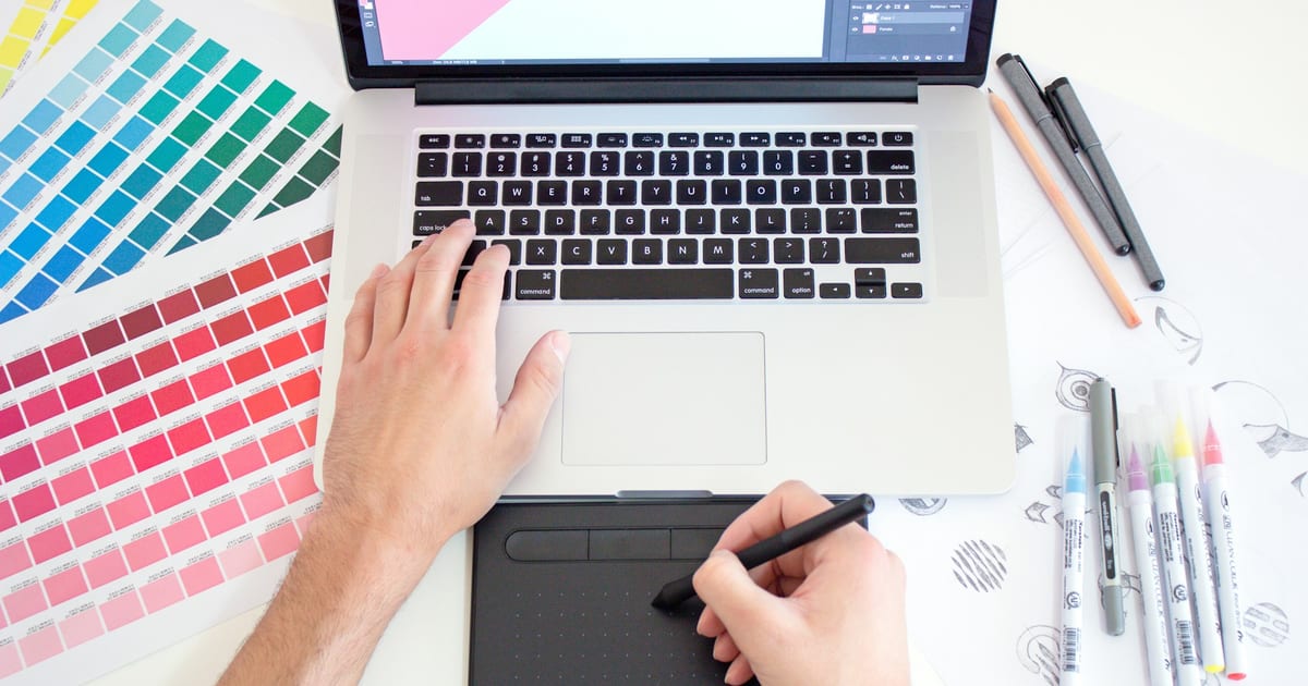 A designer working at a tablet and laptop on a studio desk.