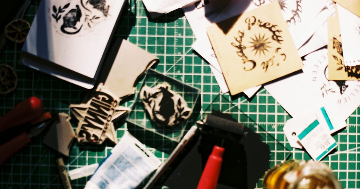 Hand-carved rubber stamps, ink and stamped paper cards spread across a cutting mat.
