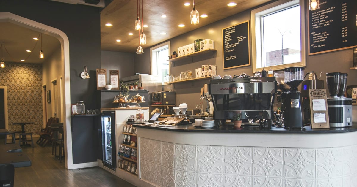 The counter of an independent coffee shop, with espresso machine, grinders and a chalk menu board.