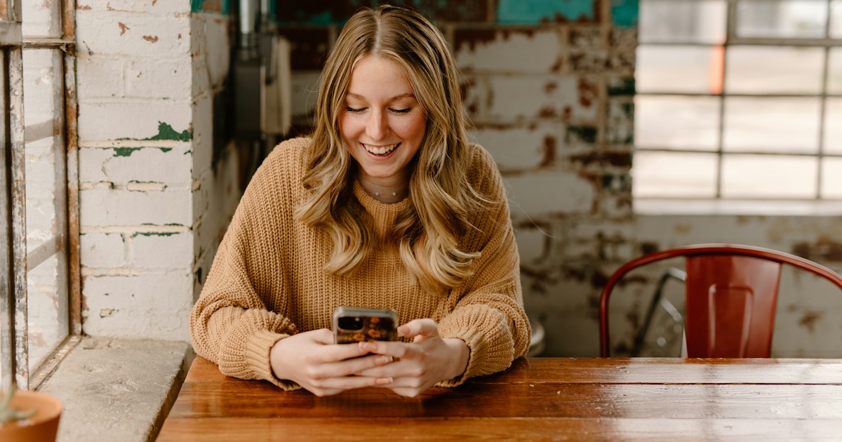 A woman sitting at a café table, looking down at her phone.