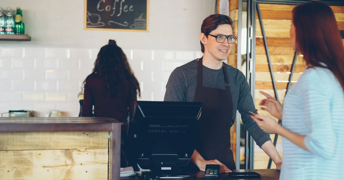 A barista chatting with a customer across the counter of a small coffee shop.