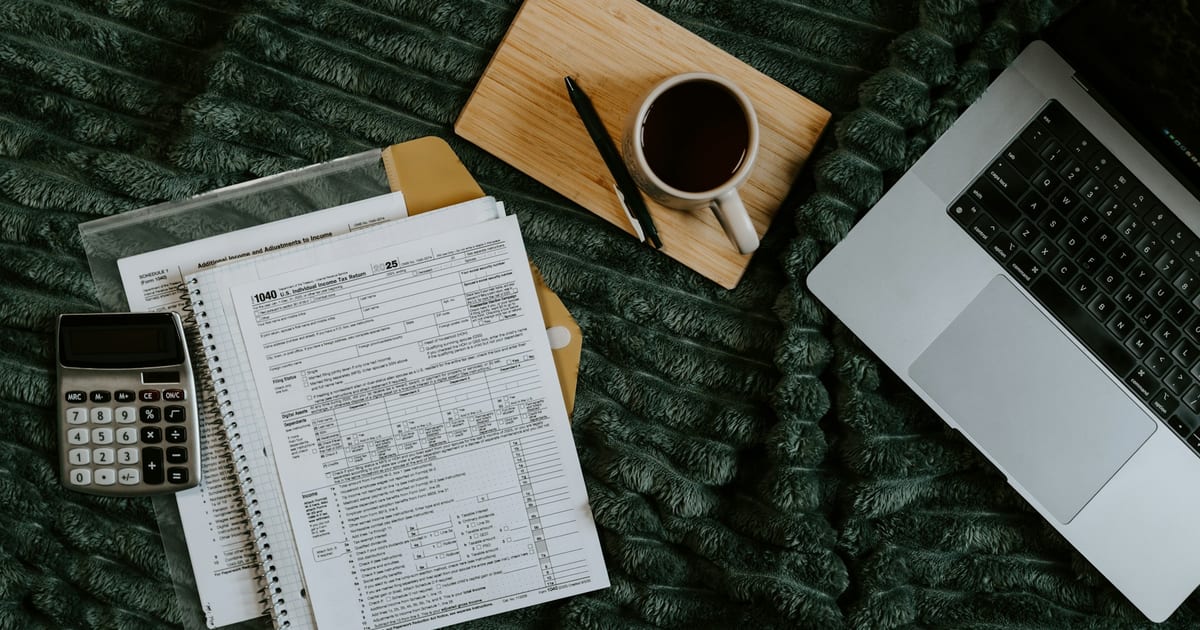 A laptop, printed figures and a calculator beside a cup of coffee.