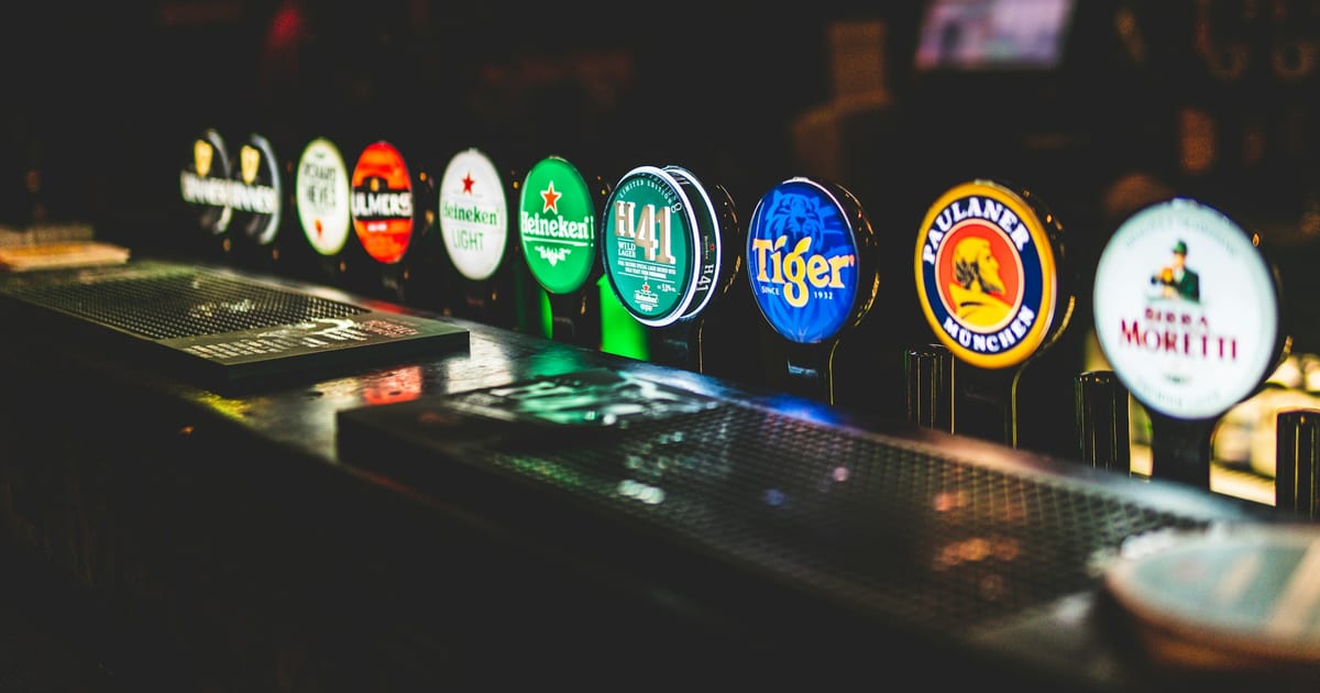 A row of illuminated beer taps along a dark pub bar.
