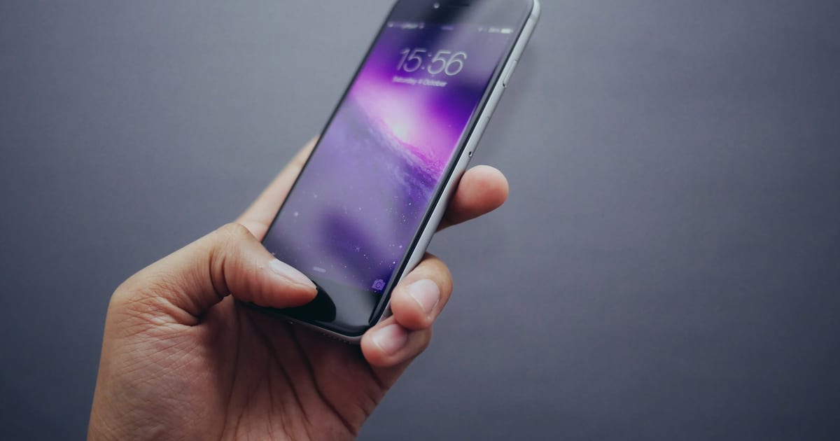 A person holding a smartphone with the screen lit in a dark room.