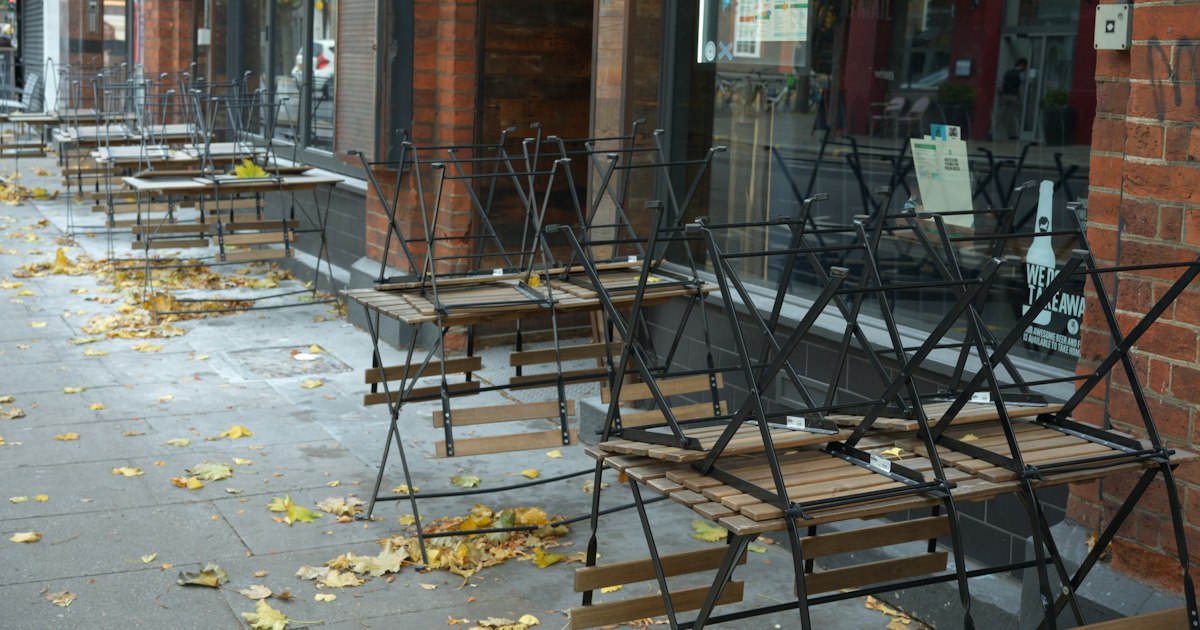 Empty outdoor café seating with fallen leaves on the ground.