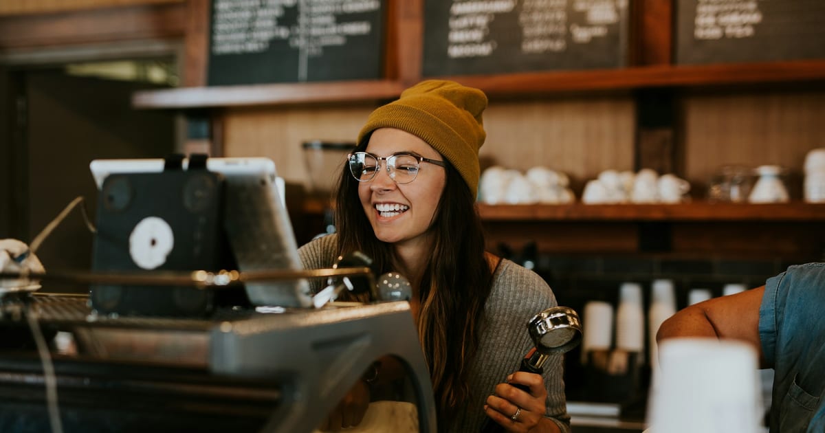 A barista at the counter of a small coffee shop, preparing a drink during a shift.