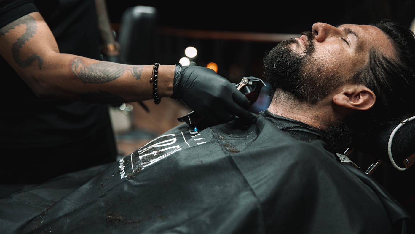 A barber trimming a customer's beard in the chair.