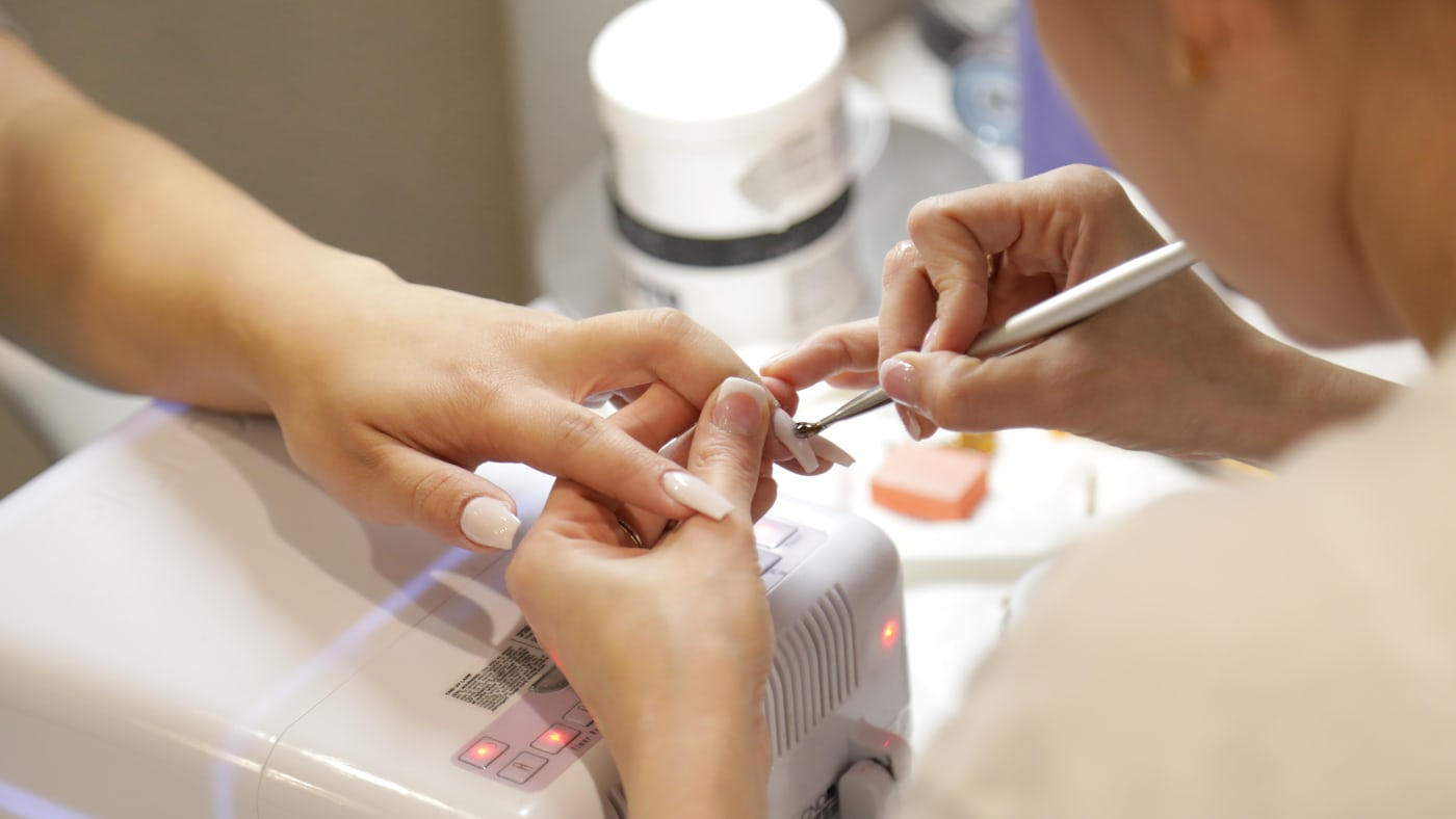 A nail technician working on a client's hands at a salon table.